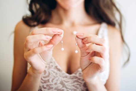 Mariée en robe de dentelle tenant délicatement des boucles d’oreilles en perles dans ses mains