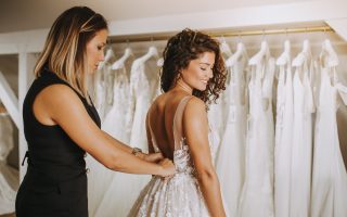 Future mariée essayant sa robe de mariée en boutique, aidée par une conseillère