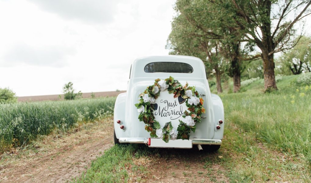 Voiture de mariage ancienne blanche décorée d'une couronne de fleurs sur un chemin de campagne
