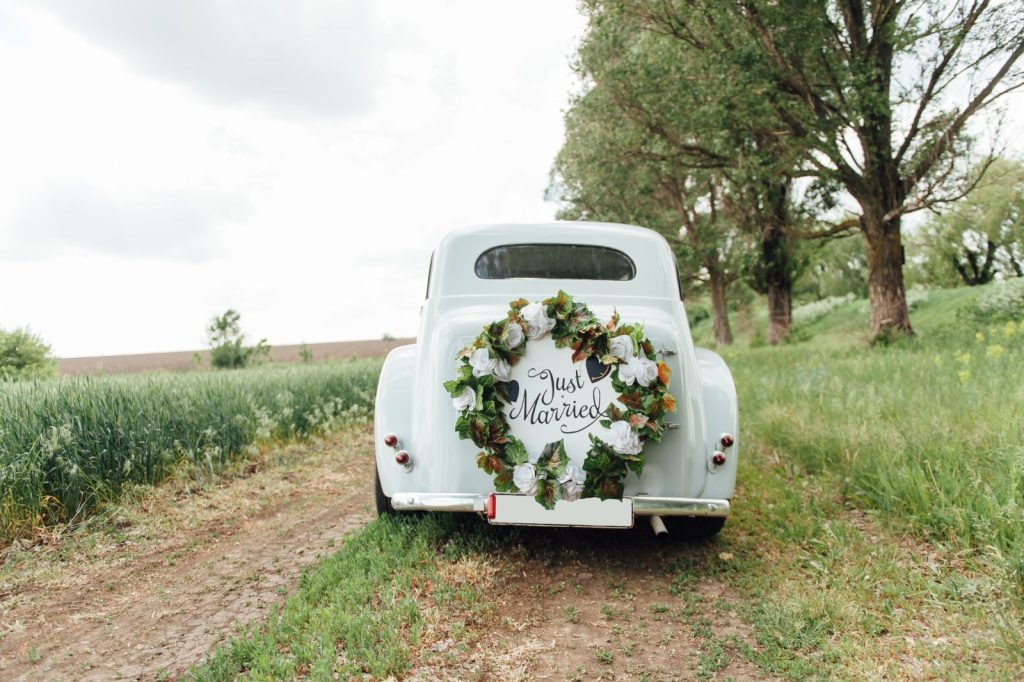 Voiture de mariage ancienne blanche décorée d'une couronne de fleurs sur un chemin de campagne