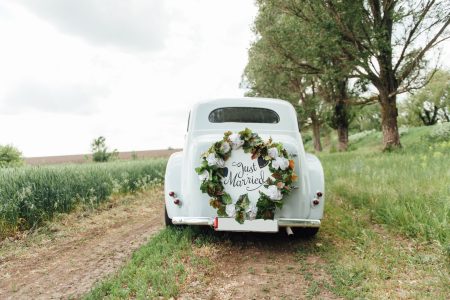 Voiture de mariage ancienne blanche décorée d'une couronne de fleurs sur un chemin de campagne