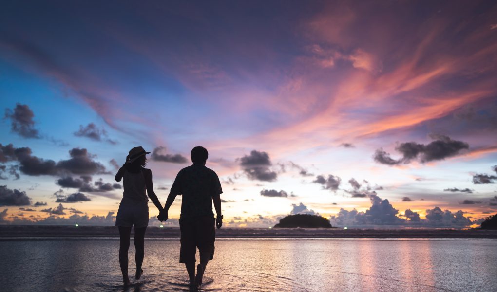 Couple main dans la main sur une plage au coucher du soleil, voyage de noces