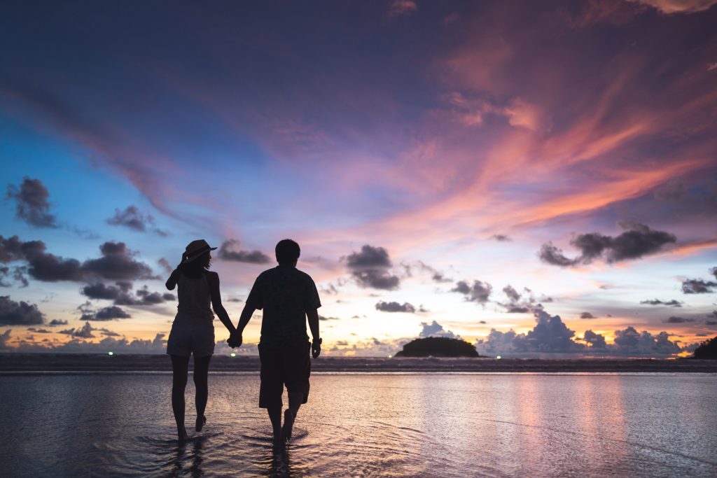 Couple main dans la main sur une plage au coucher du soleil, voyage de noces