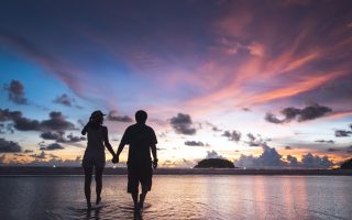 Couple main dans la main sur une plage au coucher du soleil, voyage de noces