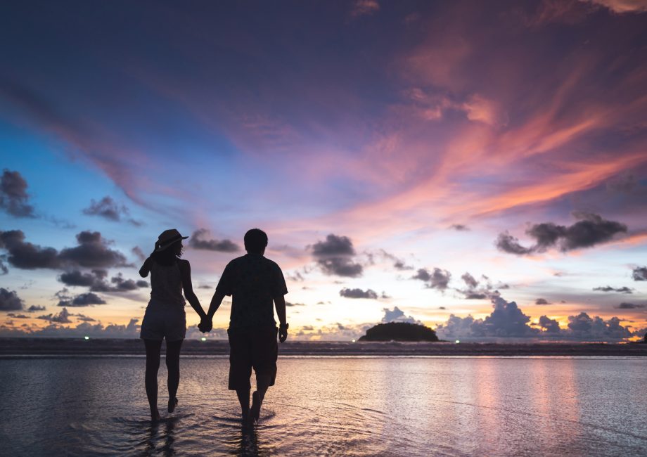 Couple main dans la main sur une plage au coucher du soleil, voyage de noces