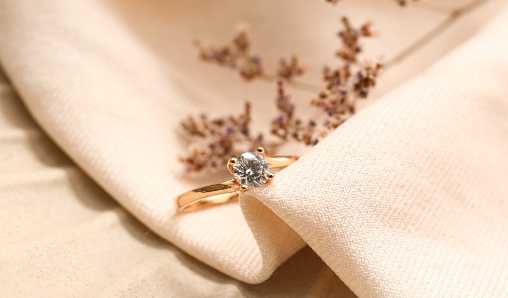 Bague de fiançailles en or rose sertie d'un diamant solitaire, posée sur un tissu beige