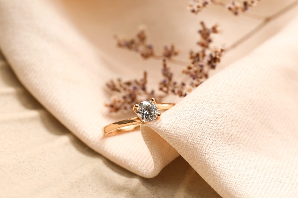 Bague de fiançailles en or rose sertie d'un diamant solitaire, posée sur un tissu beige