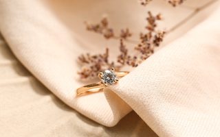 Bague de fiançailles en or rose sertie d'un diamant solitaire, posée sur un tissu beige