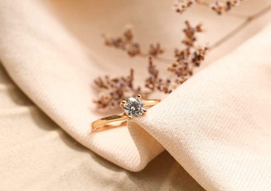 Bague de fiançailles en or rose sertie d'un diamant solitaire, posée sur un tissu beige