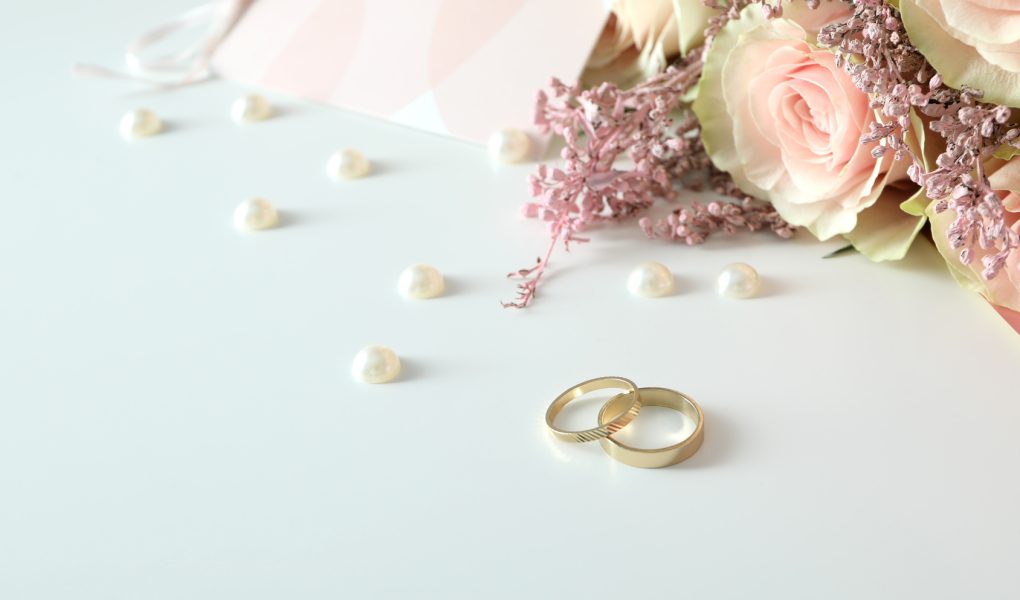 Deux alliances de mariage dorées posées sur un fond blanc avec accessoires de mariage