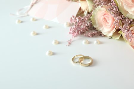Deux alliances de mariage dorées posées sur un fond blanc avec accessoires de mariage