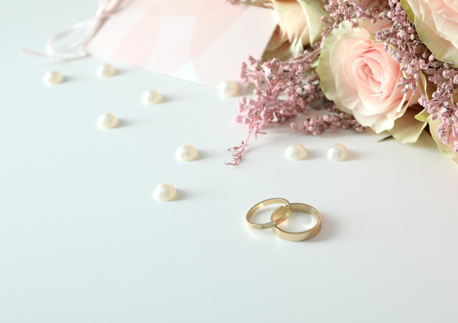 Deux alliances de mariage dorées posées sur un fond blanc avec accessoires de mariage