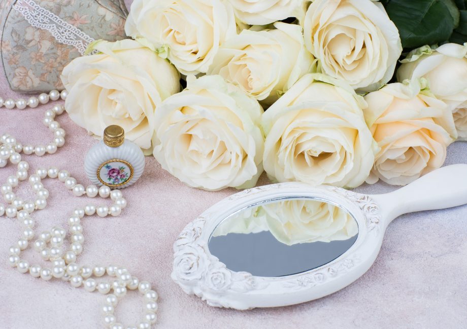 Flacon de parfum, perles et bouquet de roses blanches devant un miroir