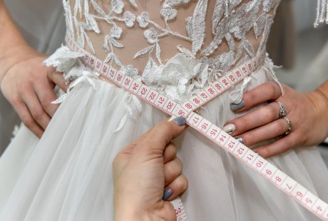 Mains tenant un mètre ruban à la taille d'une robe de mariée lors d'une retouche