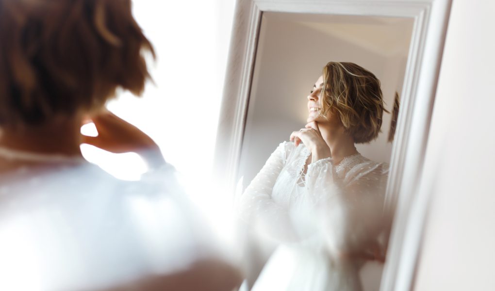 Future mariée souriante devant un miroir, dans une lumière douce du matin