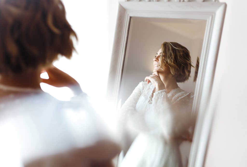 Future mariée souriante devant un miroir, dans une lumière douce du matin