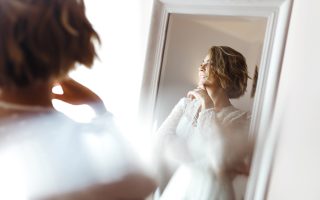 Future mariée souriante devant un miroir, dans une lumière douce du matin