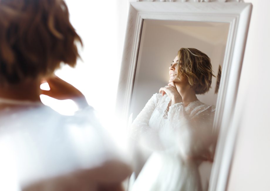 Future mariée souriante devant un miroir, dans une lumière douce du matin
